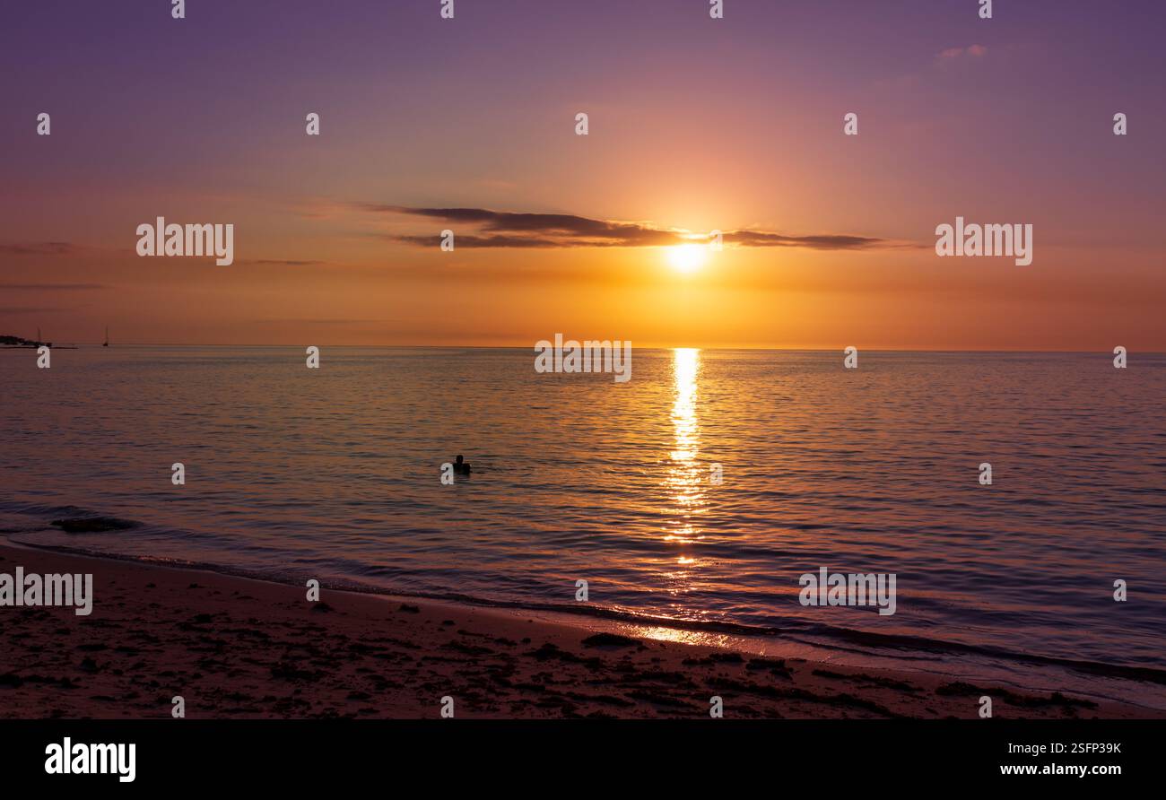 Sehr farbenfroher Sonnenuntergang über dem indischen Ozean Horizont, die Silhouette eines jungen Menschen schwimmt im Wasser in der Ferne, Mauritius Island Stockfoto