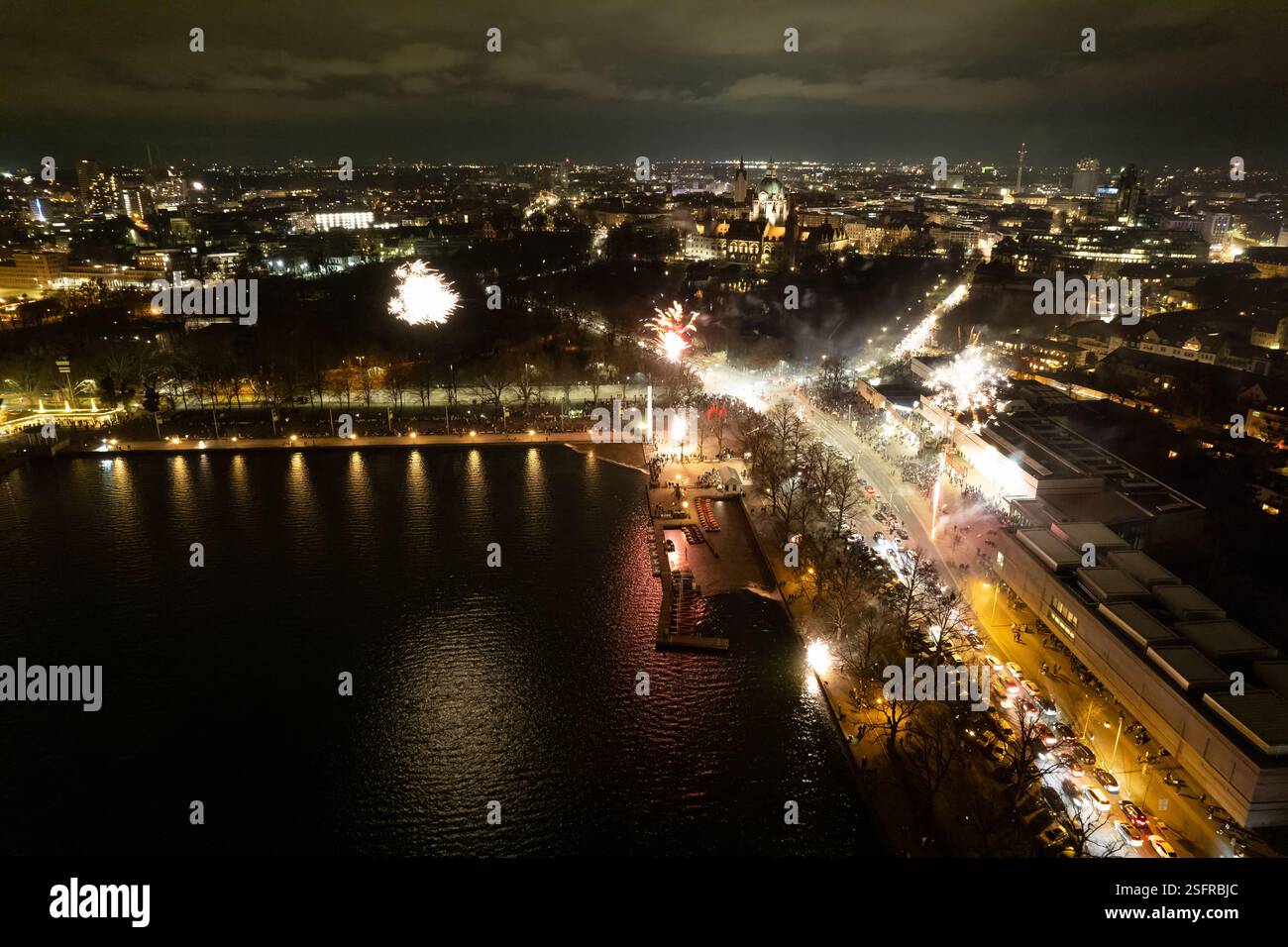 Ein atemberaubender Blick auf eine geschäftige Stadt am Wasser, beleuchtet von einem herrlichen Feuerwerk, was eine magische Feier für Hannover Maschsee Drone Neujahr 2025 FP schafft Stockfoto