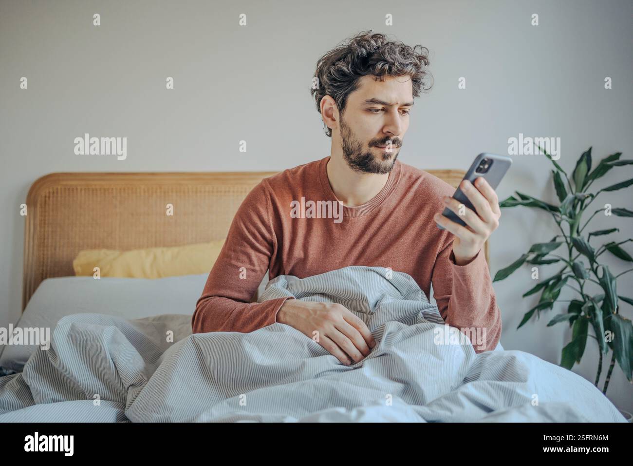 Entspannte Morgenroutine – junger gutaussehender Bärenmann aus dem Nahen Osten im Bett, der Telefon überprüft. Stockfoto