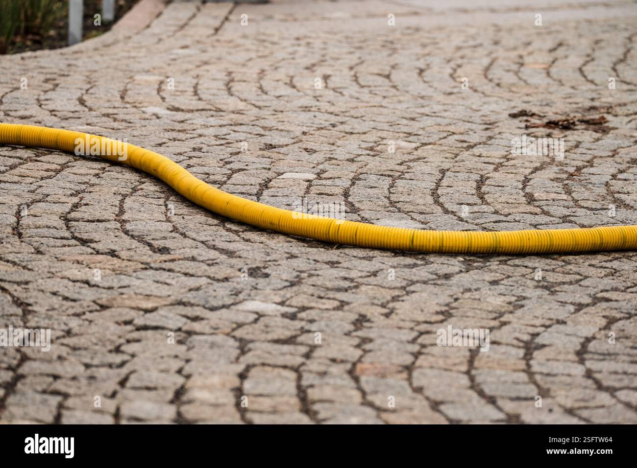 Gelber flexibler Schlauch auf Pflastersteinpflaster Stockfoto