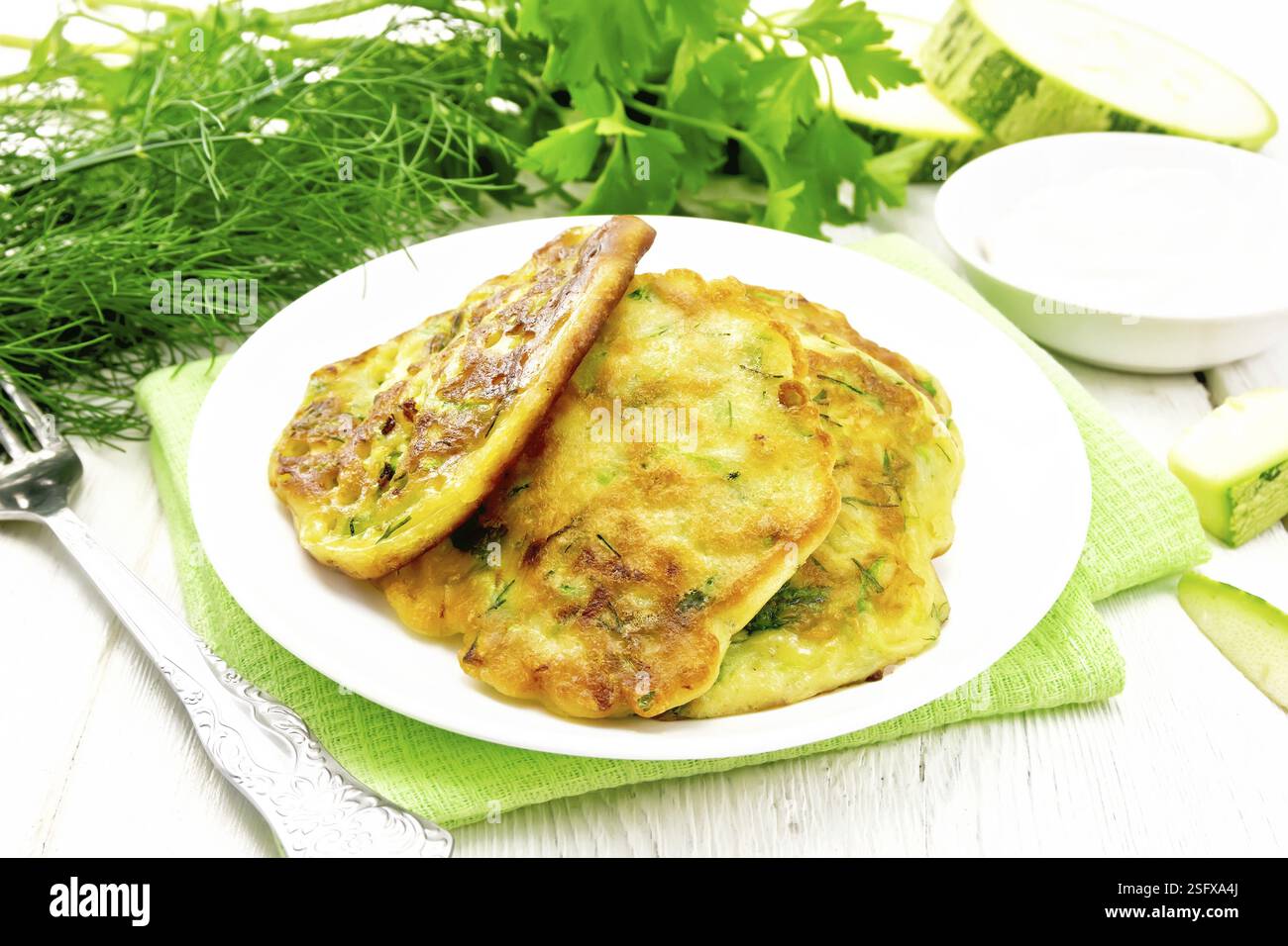 Zucchini Krapfen, Dill und Petersilie in eine Platte auf eine Serviette, saure Sahne in einer Schüssel auf dem Hintergrund des Lichts Holzbrett Stockfoto Zucchini Krapfen, Dill und Petersilie in eine Platte auf eine Serviette, saure Sahne in einer Schüssel auf dem Hintergrund des Lichts Holzbrett Stockfoto