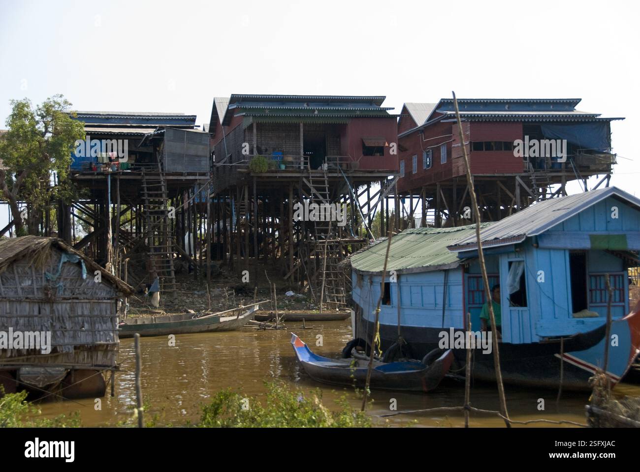 Ein blaues Hausboot liegt in der Nähe von Häusern, die auf Stelzen über dem Fluss neben dem Tonle SAP Lake gebaut wurden, der in der nassen Jahreszeit stark aufsteigt. Stockfoto