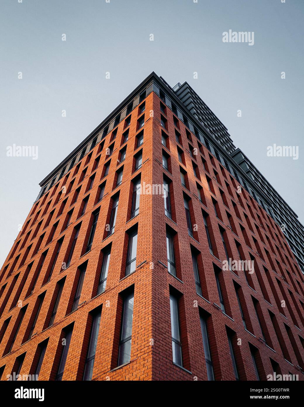 Blick auf die Fassade eines modernen Gebäudes mit Ziegelfassade. Ecke eines stilvollen Wohngebäudes bei Sonnenuntergang vor klarem blauem Himmel. Stockfoto