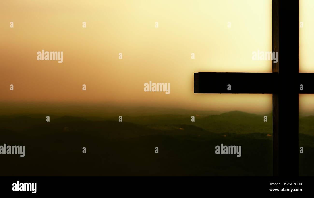 Die Silhouette eines Kreuzes vor einer trüben bergigen Landschaft bei Sonnenuntergang schafft eine ruhige und spirituelle Atmosphäre. Stockfoto