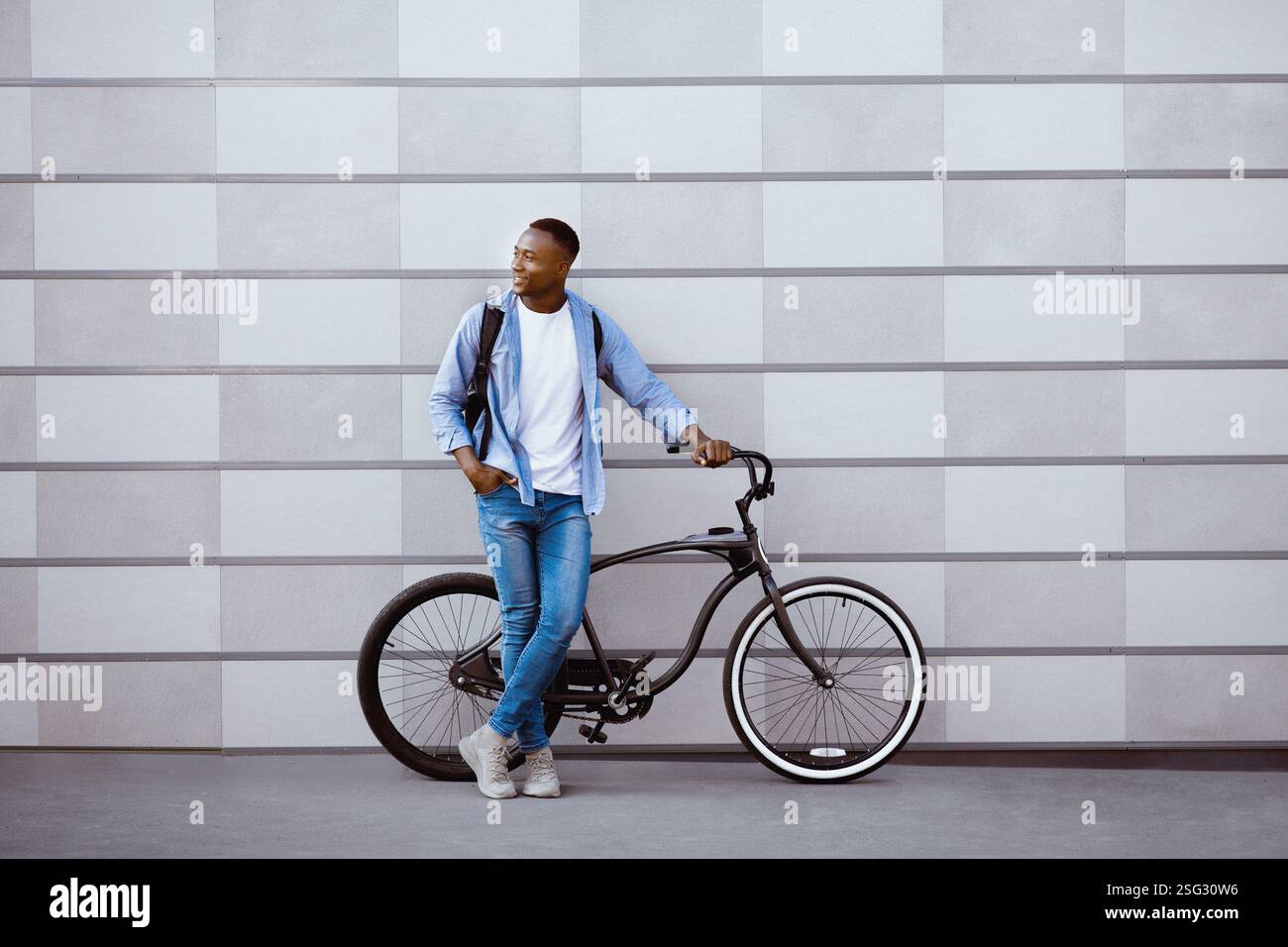 Attraktiver afroamerikanischer Kerl mit Fahrrad, das in der Nähe der Ziegelmauer auf der Stadtstraße steht, leerer Raum Stockfoto