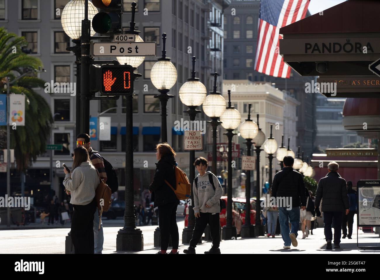 Fußgänger warten an einer Kreuzung in der Nähe der 400 Post Street in San Francisco, wo Pandora und Victoria's Secret Stores sichtbar sind. Fußgängersignal leuchtet rot. Stockfoto