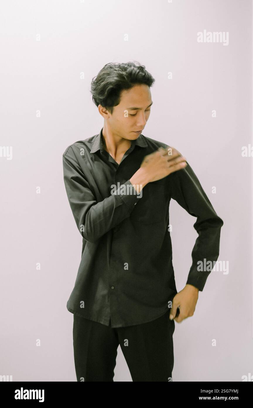 Stilvoller Mann, der sein schwarzes Hemd vor einem einfarbigen Hintergrund glättet. Stockfoto
