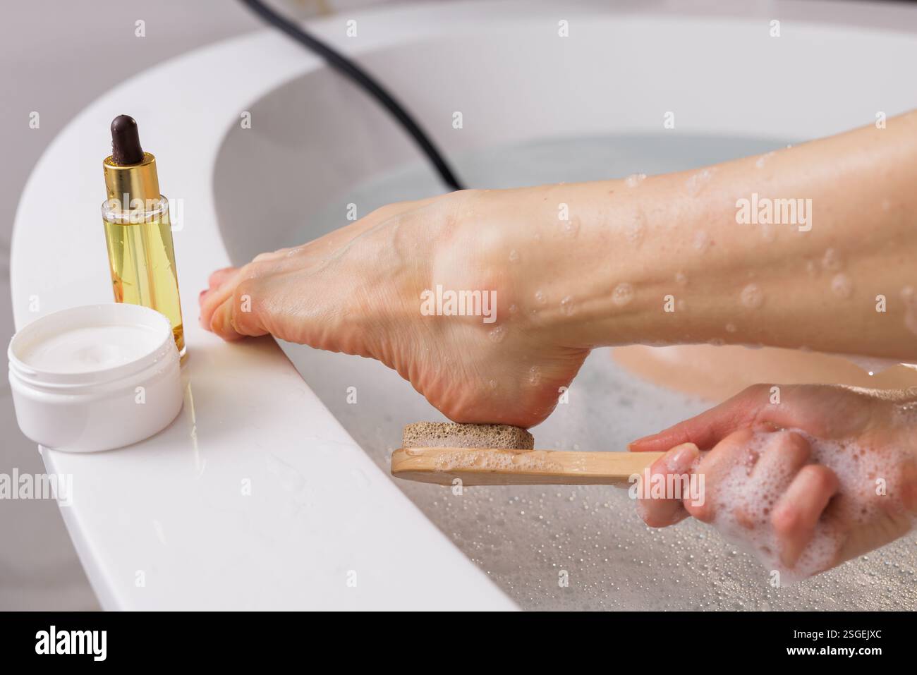 Fußpflege und Entspannung. Frau, die den Fuß mit einem Bimsstein in einem warmen Bad peelt. Hautpflegeprodukte wie Creme und Öl in der Nähe. Spa, Selbstversorgung, an Stockfoto