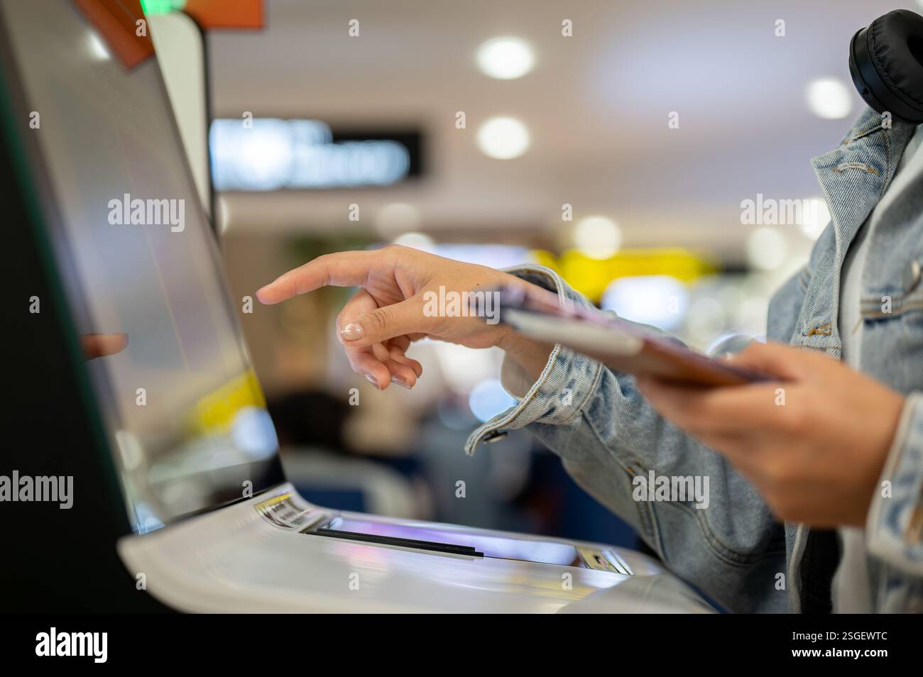 Ein Nahbild der Hand: Eine Passagierin checkt für ihren Flug an einem Selbsteincheckautomaten im Flughafenterminal ein, mit einem Finger auf o Stockfoto
