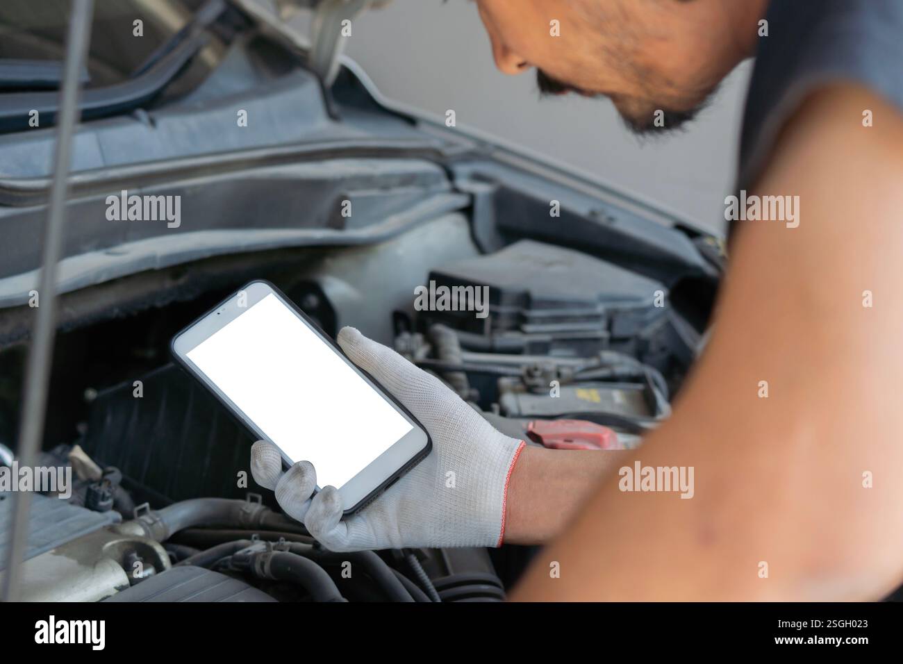 Techniker überprüft den Motor des Autos und hält das Smartphone mit isoliertem Bildschirm. Autoservice, Reparatur, Reparatur. Kopierbereich. Stockfoto