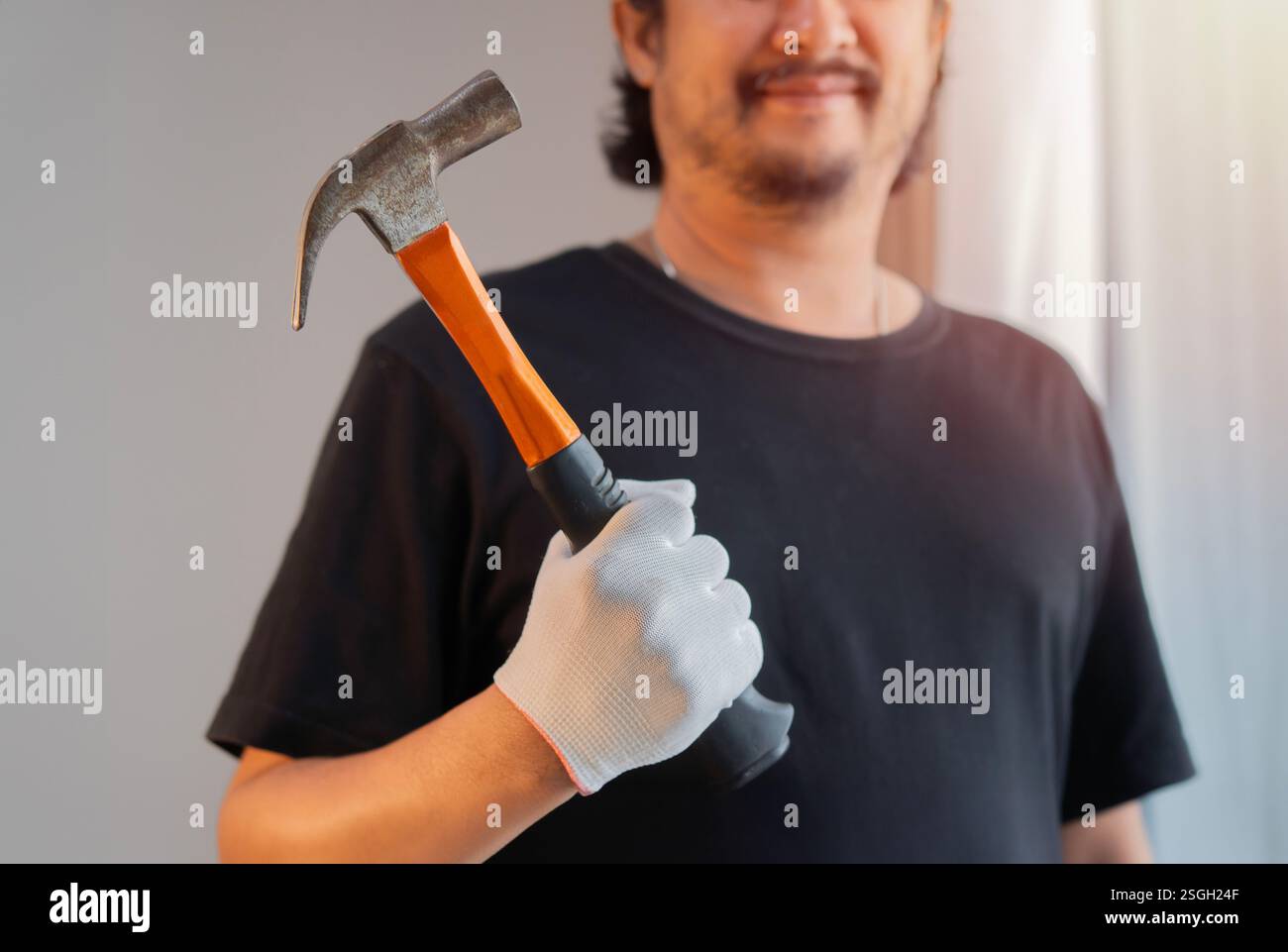 Abgeschnittener Schuss eines gutaussehenden asiatischen Mannes in schwarzem T-Shirt, der einen Hammer zu Hause hält. Selektiver Fokus. Stockfoto