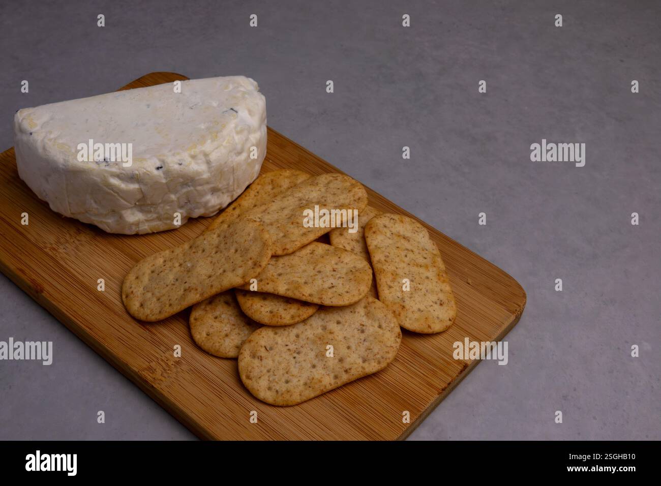 Weichkäse und knusprige Cracker auf einem Holzbrett sorgen für einen einladenden Snack, der perfekt für Versammlungen oder entspannte Genüsse ist. Stockfoto