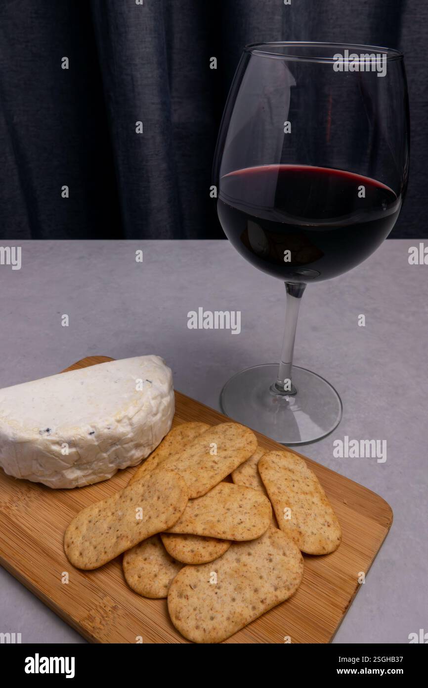 Die gemütliche Einrichtung umfasst ein Glas Rotwein, eine Portion Käse und Cracker auf einem Holzbrett, perfekt zum Entspannen am Abend. Stockfoto