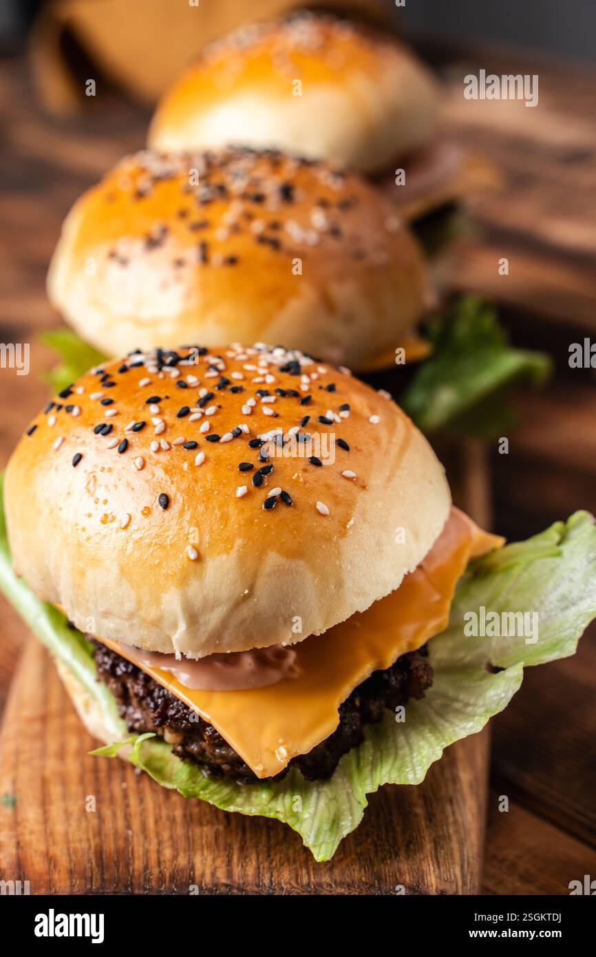 Drei Burger mit Patty, Käse und Salat auf Holzbrett und Hintergrund. Nahaufnahme. Hochwertige Fotos Stockfoto