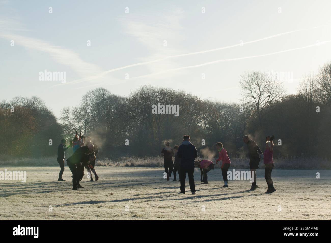 Eine Gruppe von Menschen nimmt an einem Outdoor-Fitnesstraining auf einem frostigen Feld Teil, umgeben von Bäumen und einem klaren Himmel. Sale Water Park, Manchester, Großbritannien Stockfoto