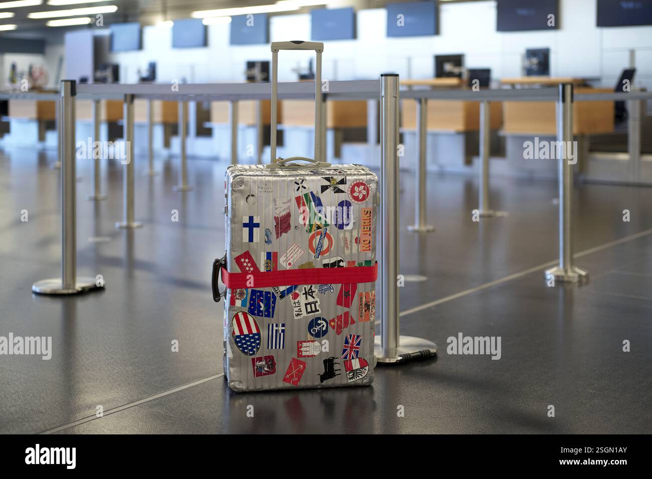 Der mit Reiseaufklebern bedeckte Koffer steht am leeren Check-in-Schalter am Flughafen Stockfoto