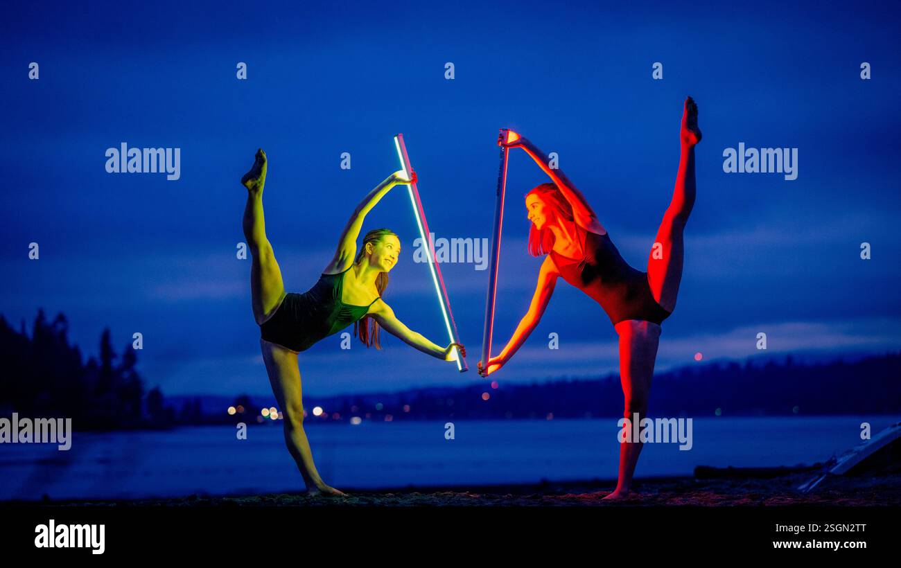 Zwei Frauen spielen bei Nacht in den USA eine flexible Tanzposition mit beleuchteten Stöcken am See Stockfoto