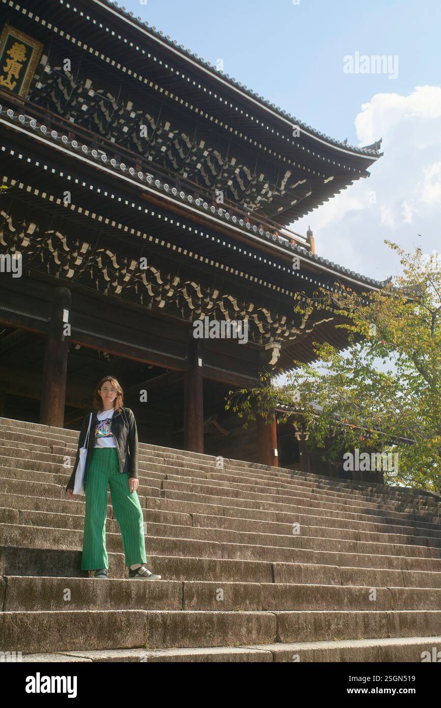 Frau in grüner Hose steht auf Steintreppen, die zu einem kunstvollen traditionellen Tempel führen. Kyoto, Japan Stockfoto