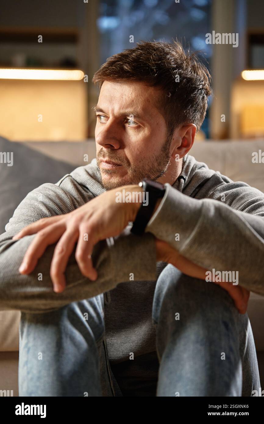 Ein Mann mittleren Alters sitzt allein zu Hause und blickt mit nachdenklichem Ausdruck weg. Vorstellung von Introspektion, tiefem Denken und emotionaler Reflexion Stockfoto