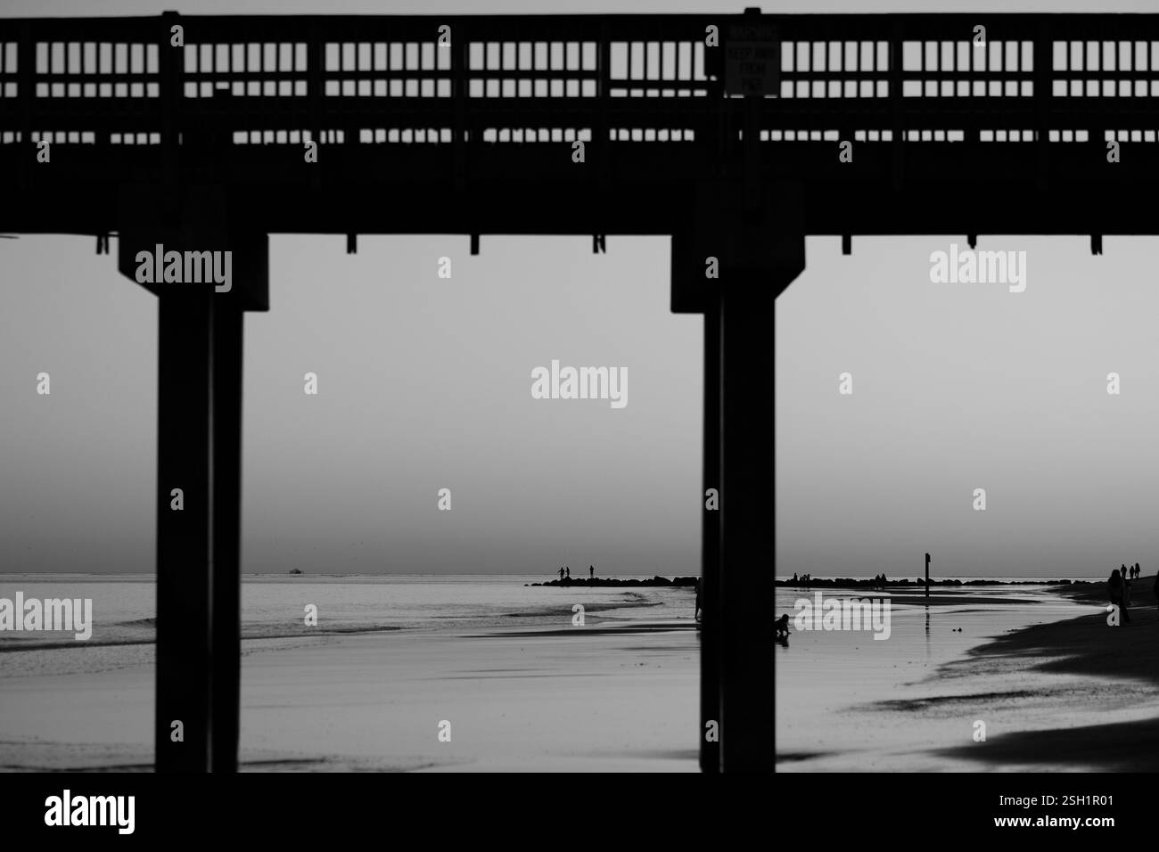 Spektakulärer Sonnenuntergang am Ozean mit lebendigem Himmel, Strandsilhouetten und Pier-Rahmen Stockfoto