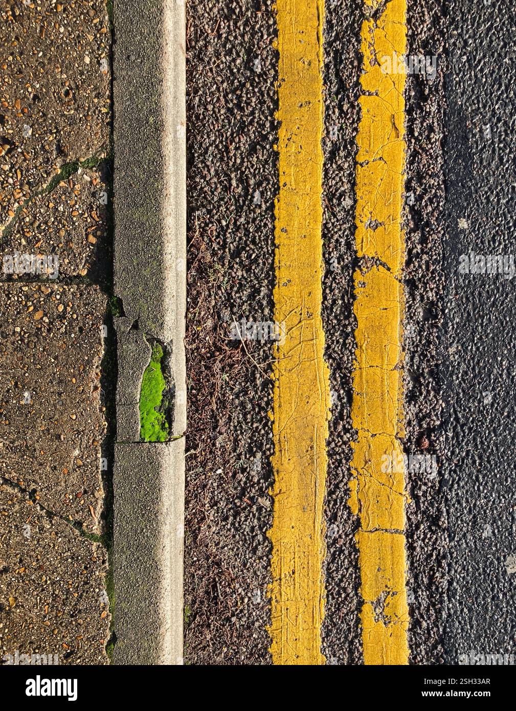 Foto mit Blick nach unten auf den Rand eines Bürgersteigs, mit doppelten gelben Linien auf der Straße nach rechts und dem Bürgersteig und der Bordsteinkante nach links. Teil von Th - Smartphone-aufgenommenes Stockfoto