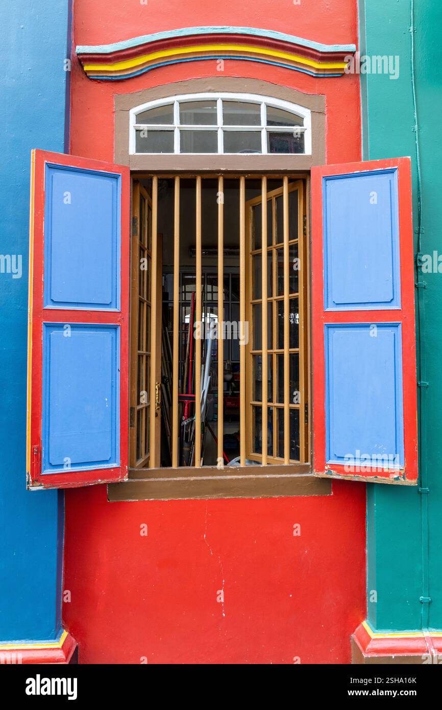 Farbenfrohe Gebäudefassade, offenes Fenster mit Holzstangen und blauen Fensterläden. Stockfoto
