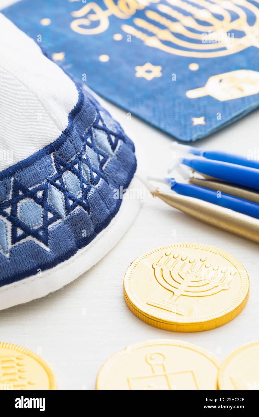 Eine weiße und blaue Garnmulke mit Goldmünzen, Kerzen und Serviette für die Hanukkah-Feier auf weißem Holzhintergrund Stockfoto