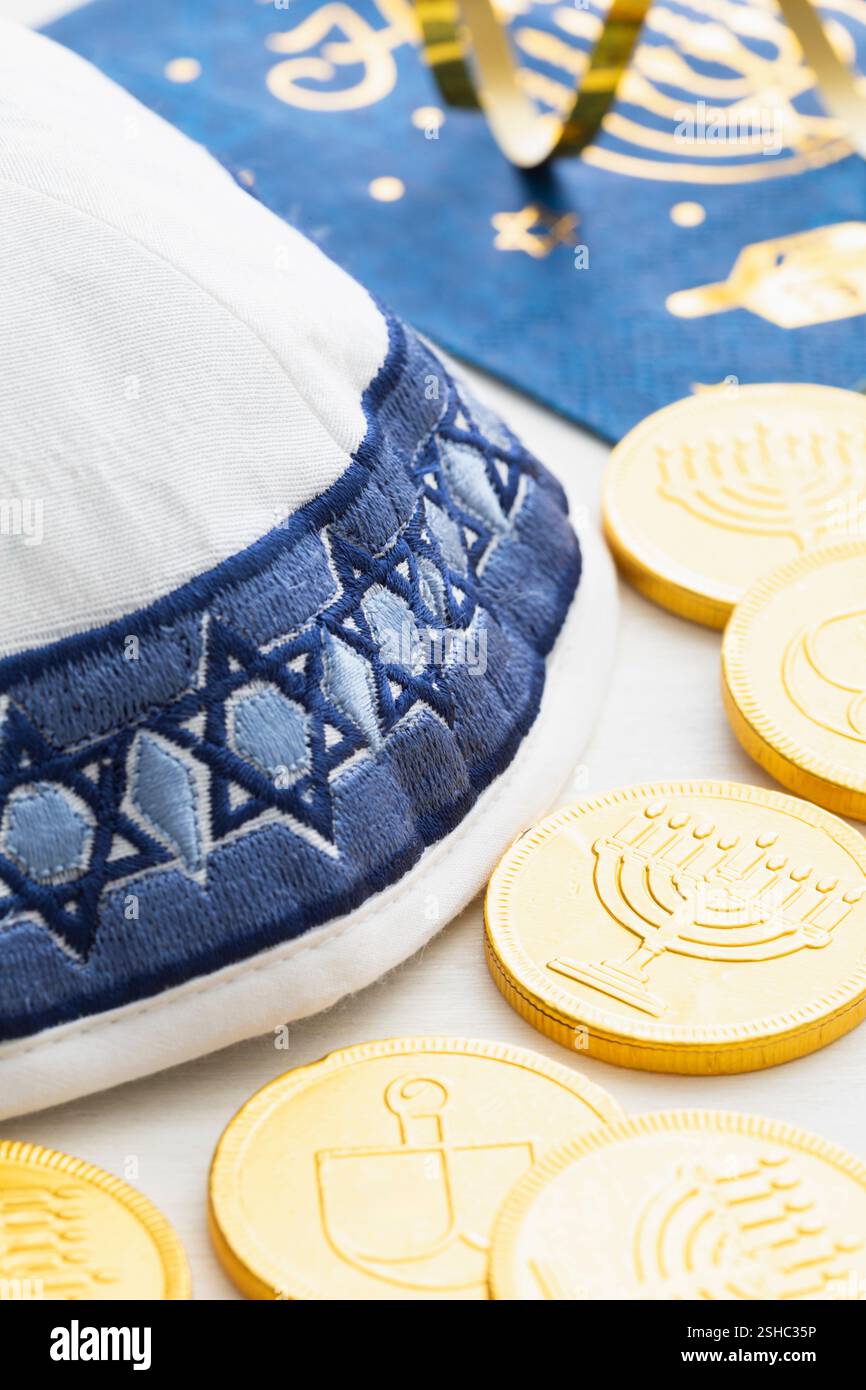 Eine weiße und blaue Garnmulke mit Goldmünzen und Serviette für die Hanukkah-Feier auf weißem Holzhintergrund Stockfoto