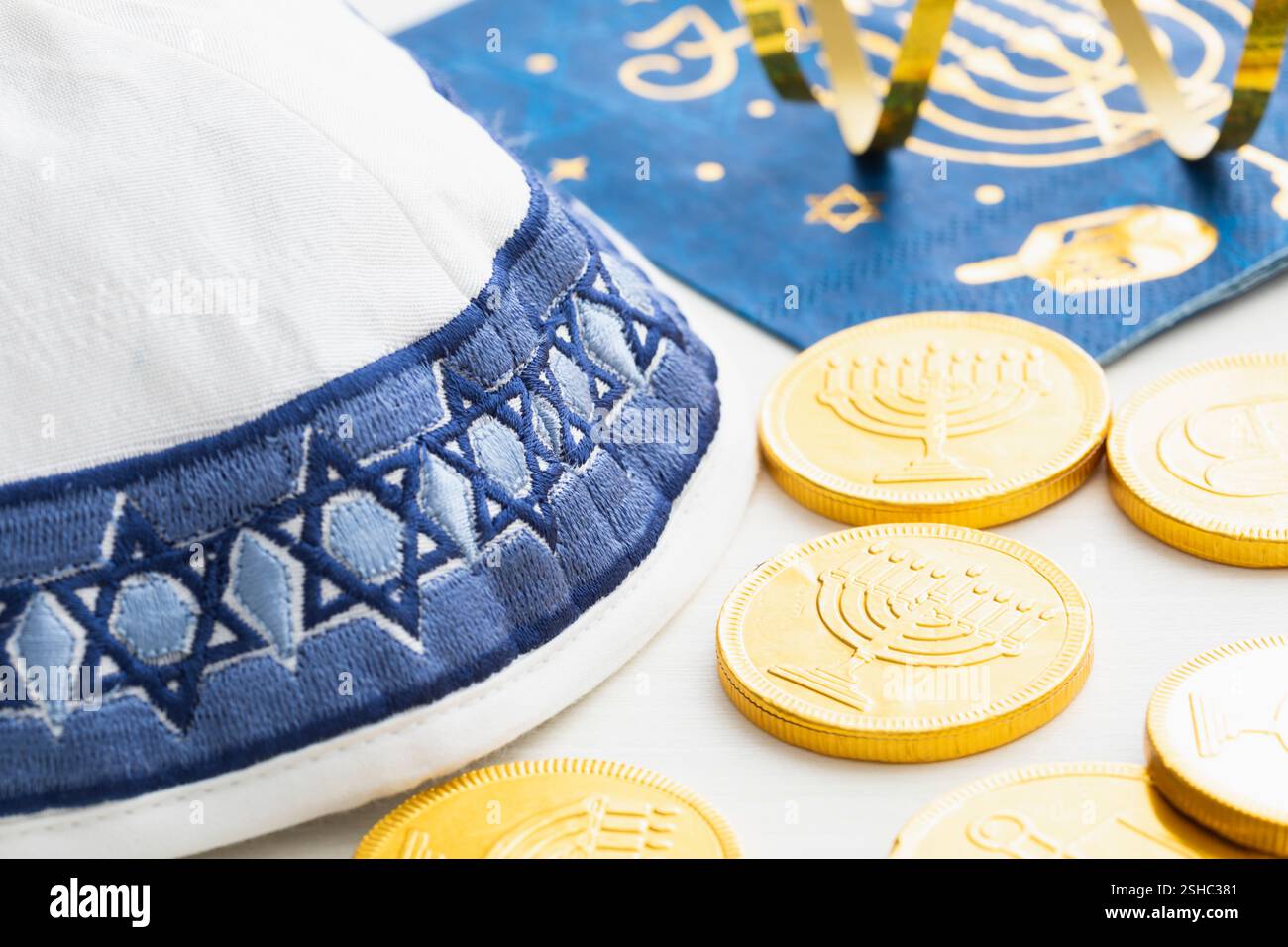 Eine weiße und blaue Garnmulke mit Goldmünzen und Serviette für die Hanukkah-Feier auf weißem Holzhintergrund Stockfoto
