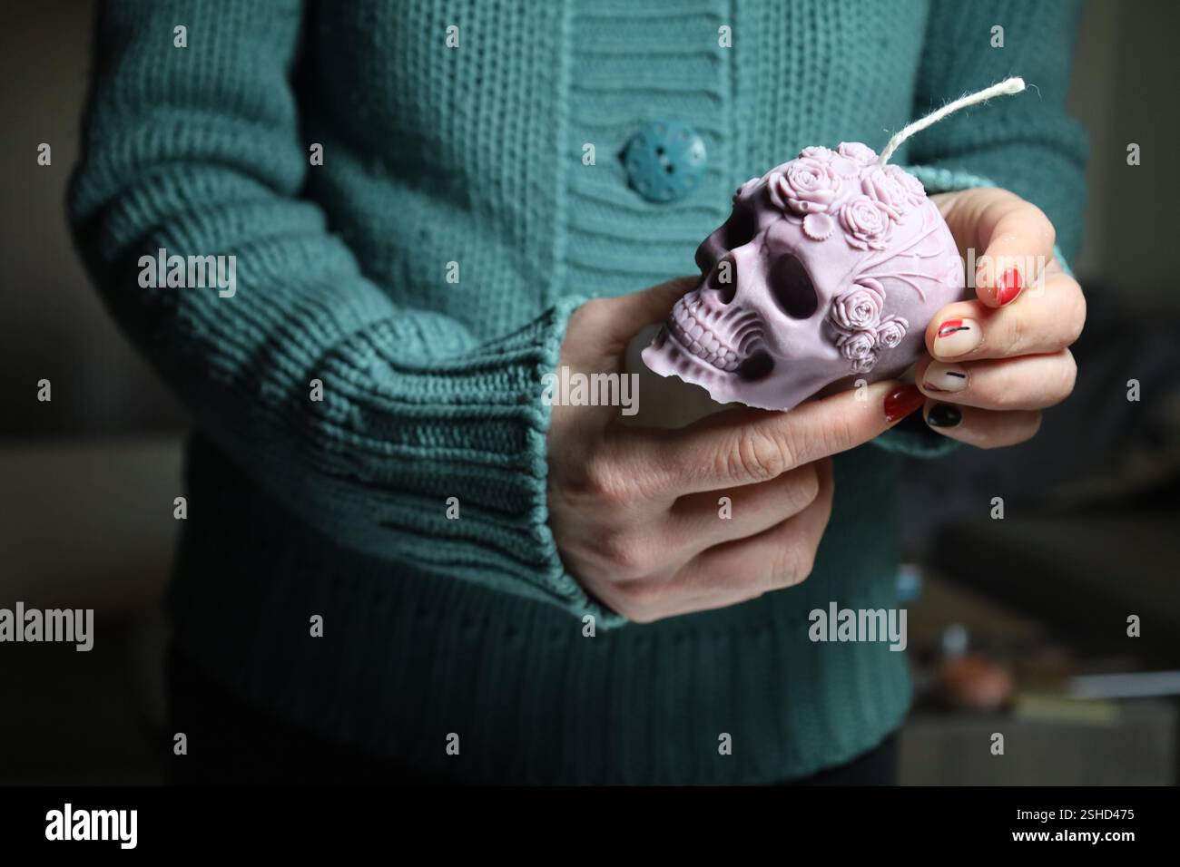 Junge Frau mit einer dekorativen, hellvioletten Kerze in Form eines Schädels mit Blumenmotiven. Stockfoto