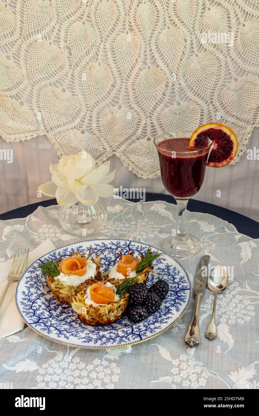 Knuspriges Kartoffelnest mit Ziegenkäse und Lachslauch mit schwarzen Beeren und einer Blutorangenmimosa auf einem formellen Tisch. Stockfoto