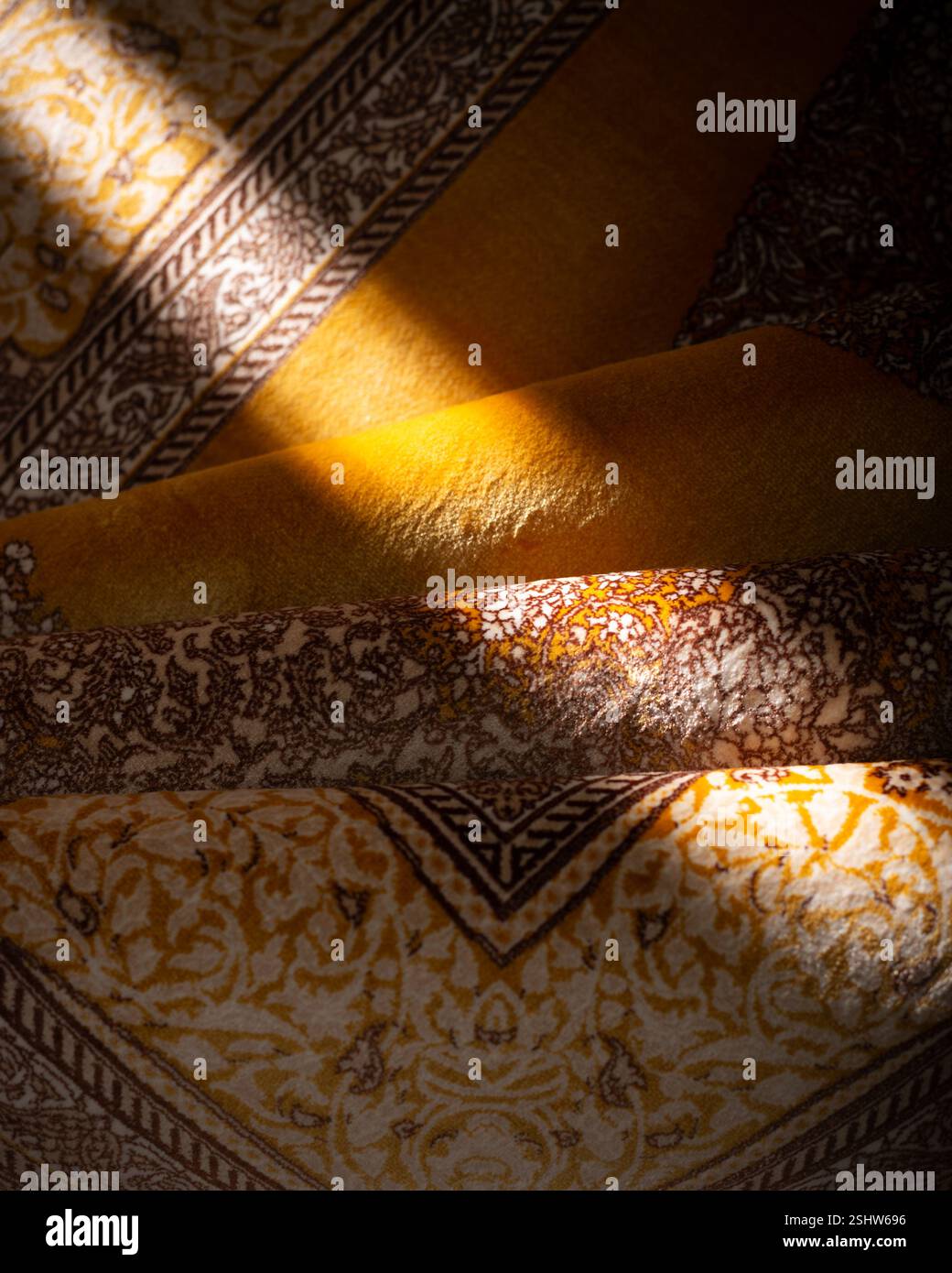 Sonnendurchfluteter traditioneller Stoff mit komplizierten Mustern, kräftigen Gelb- und Brauntönen in einer strukturierten, mehrschichtigen Komposition Stockfoto