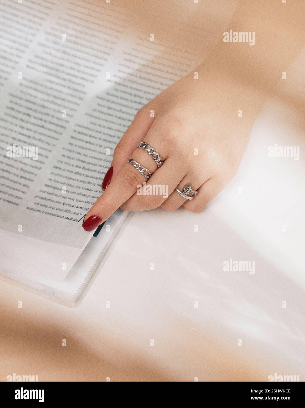 Nahaufnahme einer Frauenhand mit rotem nagellack, die eine Seite in einem Magazin dreht und stilvolle Silberringe zeigt Stockfoto