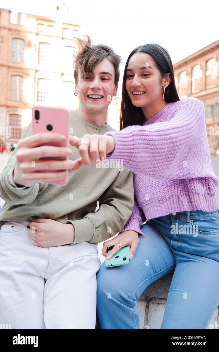 Vertikal. Fröhliche junge Freunde, die mit ihren Handys interagieren, während sie spannende Momente und Lachen teilen. Teenager konzentrierten sich auf ihr Mobiltelefon, genossen Erlebnisse und schufen gemeinsam Verbindungen. Hochwertige Fotos Stockfoto