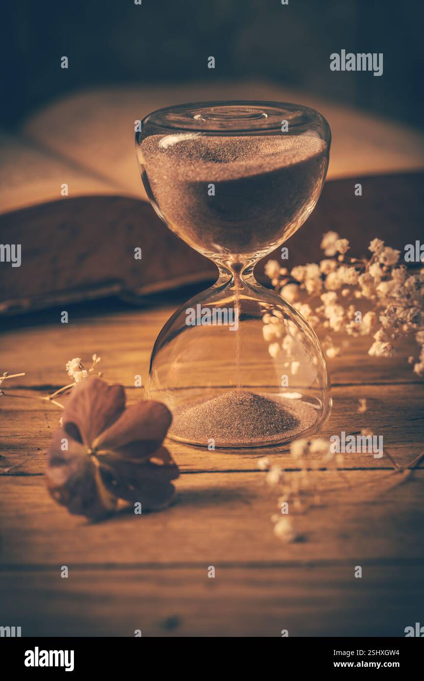 Sanduhr mit altem Buch. Symbol für vergangene Zeit und Erinnerungen. Konzeptionelles Vintage-Image Stockfoto