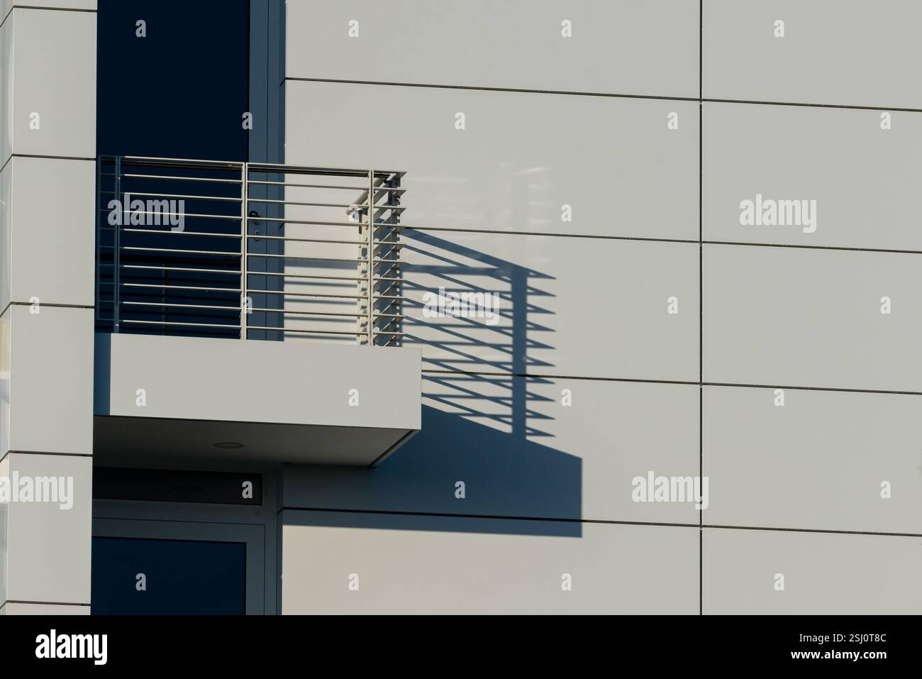 Ein modernes Gebäude verfügt über einen eleganten Balkon mit einem Geländer, das komplexe Schatten auf die helle Wand darunter wirft. Der Kontrast hebt Archi hervor Stockfoto