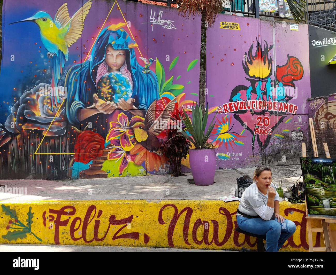 Frau sitzt vor Graffiti an einer Wand in Comuna 13, Medellin, Antioquia, Kolumbien Stockfoto