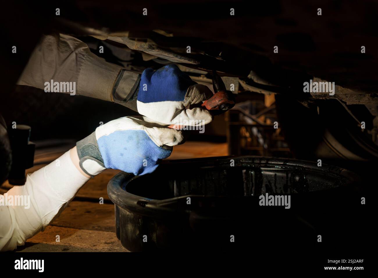 Mechaniker, der unter dem Fahrzeug mit Werkzeugen in Dimmerbeleuchtung arbeitet. Stockfoto