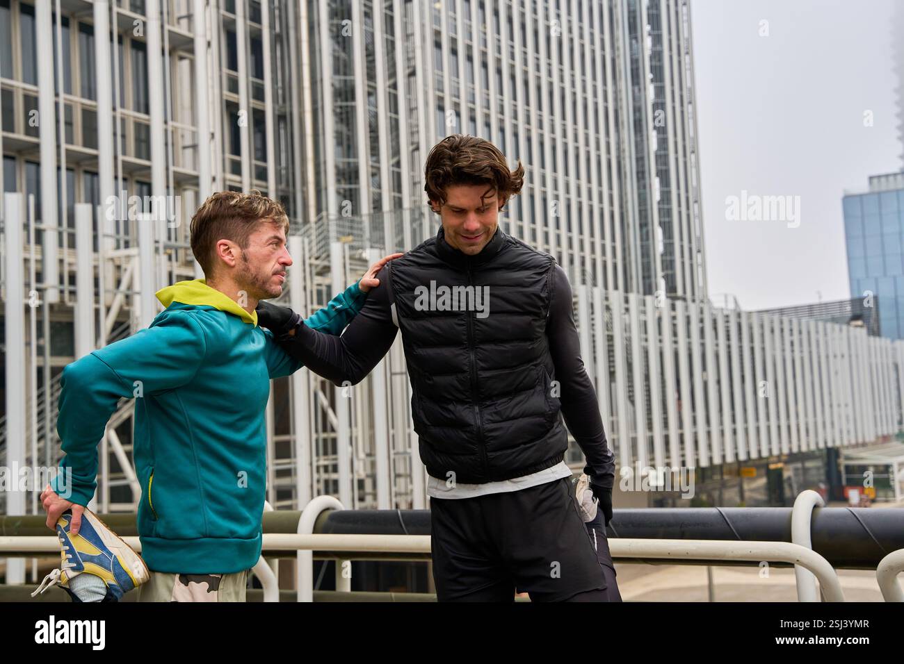 Zwei männliche Athleten, die ihre Beine nach dem Training im Freien in einer modernen urbanen Umgebung Strecken Stockfoto