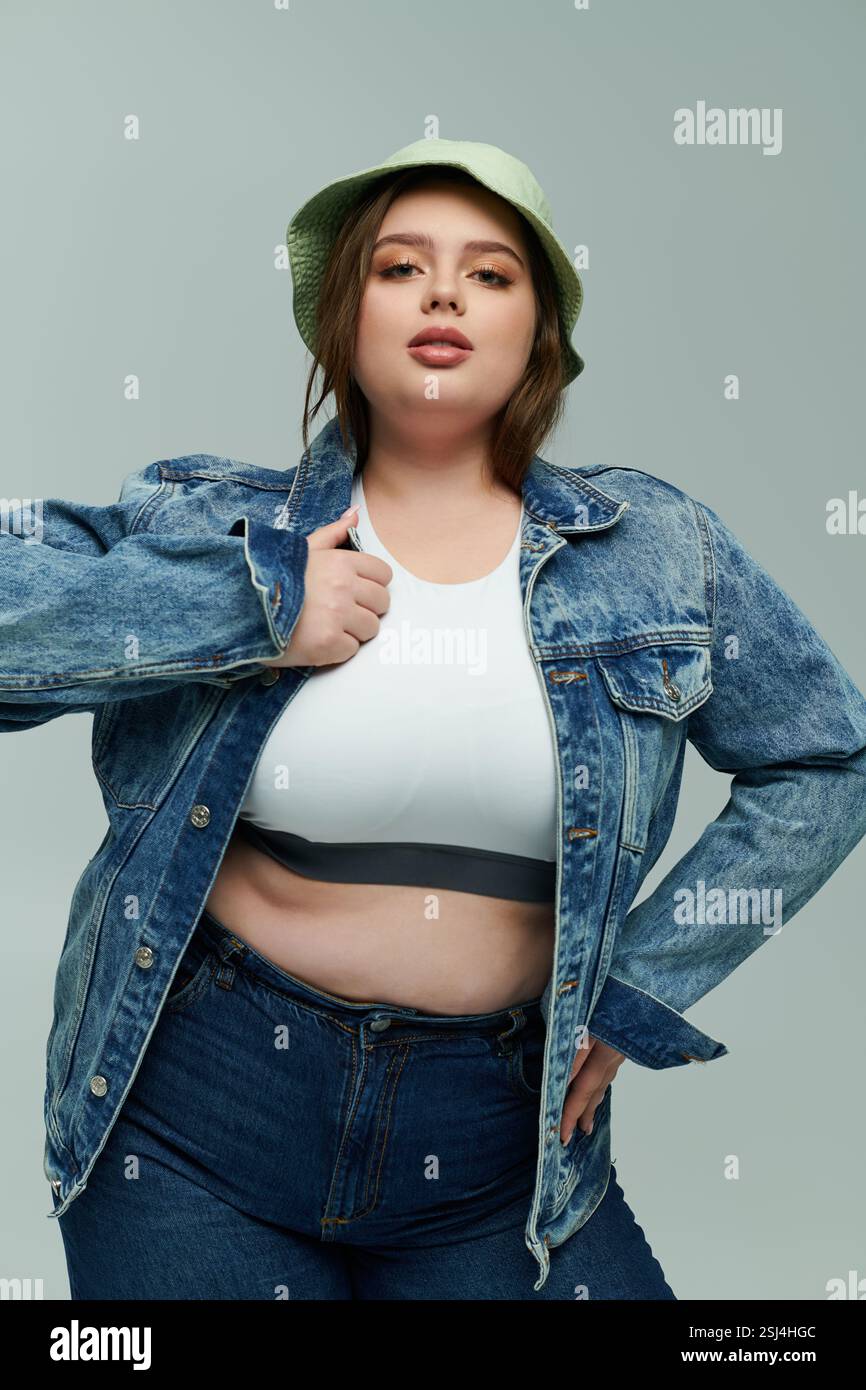 Eine junge Frau in Übergröße zeigt selbstbewusst ihren Sinn für Mode in einer Jeansjacke und -Mütze. Stockfoto
