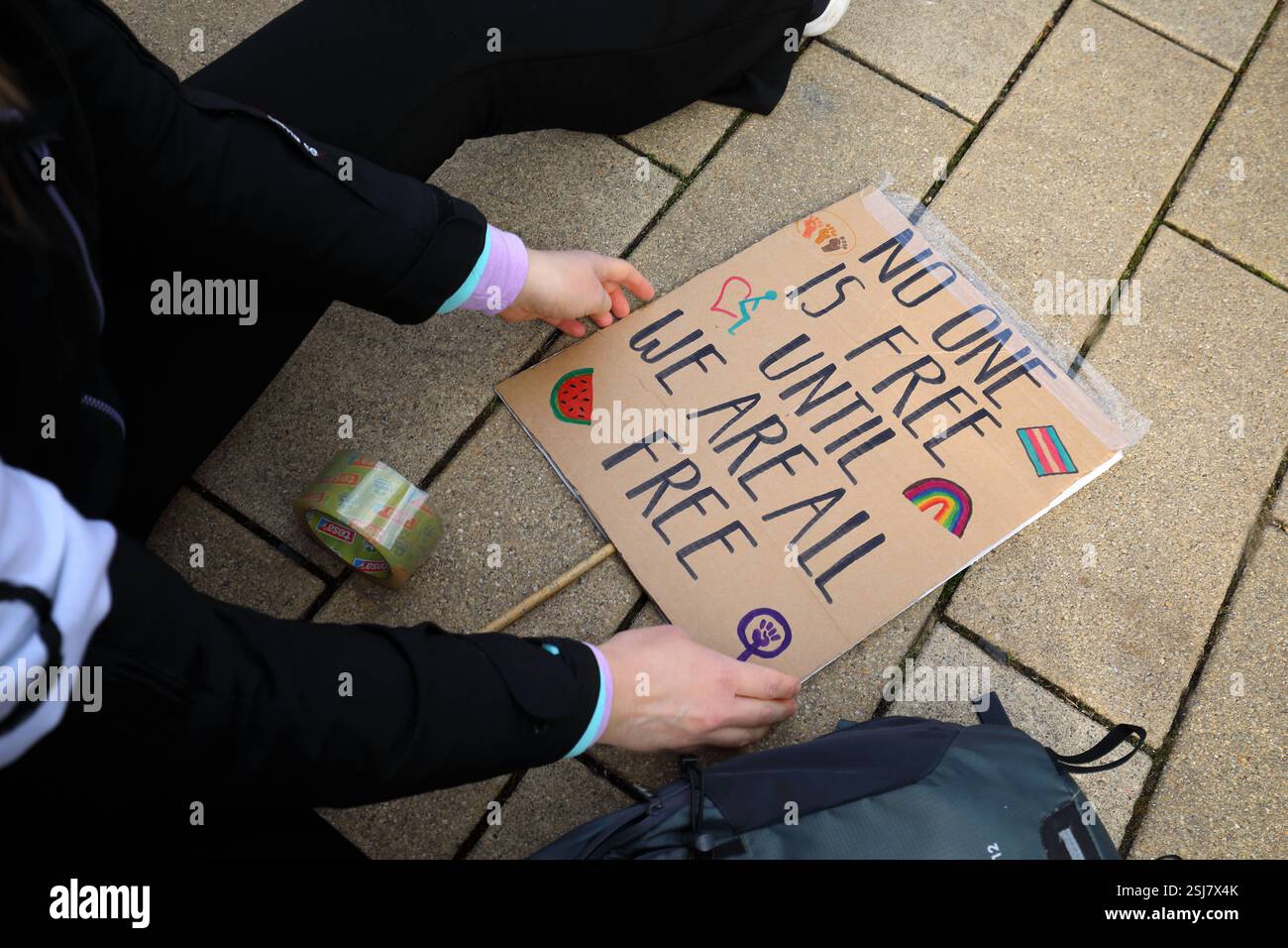 Unter dem Titel nie wieder ist jetzt - Großdemonstration gegen den Rechtsruck in der Gesellschaft - Demoschild: NIEMAND IST FREI BIS WIR ALLE FREI SIND Abbildung: Regenbogen trans Pride Flagge Feminismus Symbol - Deutschland, DE, DEU, Deutschland, Gießen, 08.02.2025: Protestaktion gegen rechte Tendenzen und den gesellschaftlichen Rechtsruck in weiten Teilen der Deutschen Bevölkerung. Ein weiteres aktuelles Thema war die Abstimmung von Union, FDP und AfD im Deutschen Bundestag zur Migrationsdebatte. Die Protestierenden zeigen ihren Unmut gegen den Kanzlerkandidaten der CDU Friedrich Merz auf zahlre Stockfoto
