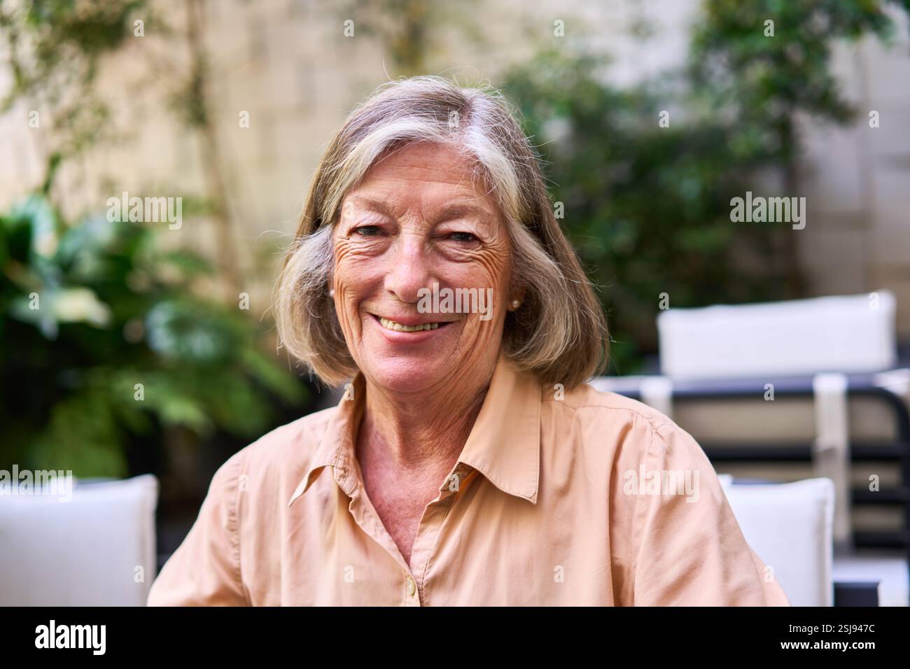 Eine fröhliche Seniorin mit grauen Haaren, die draußen sitzt, genießt die ruhige Atmosphäre inmitten von Grün und strahlt Glück und Entspannung aus Stockfoto