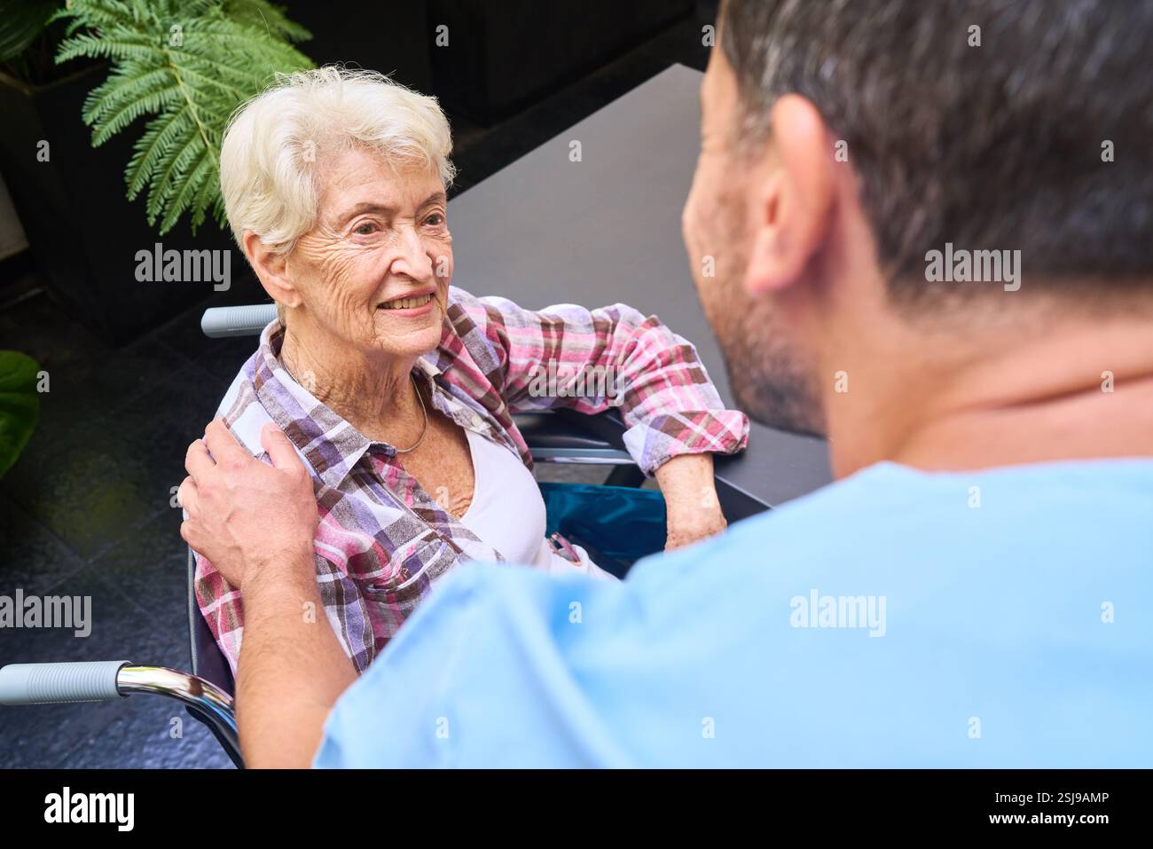 Freundliche Interaktion in einer Seniorenpflegeeinrichtung mit einer Pflegeperson, die eine ältere Frau unterstützt. Stockfoto