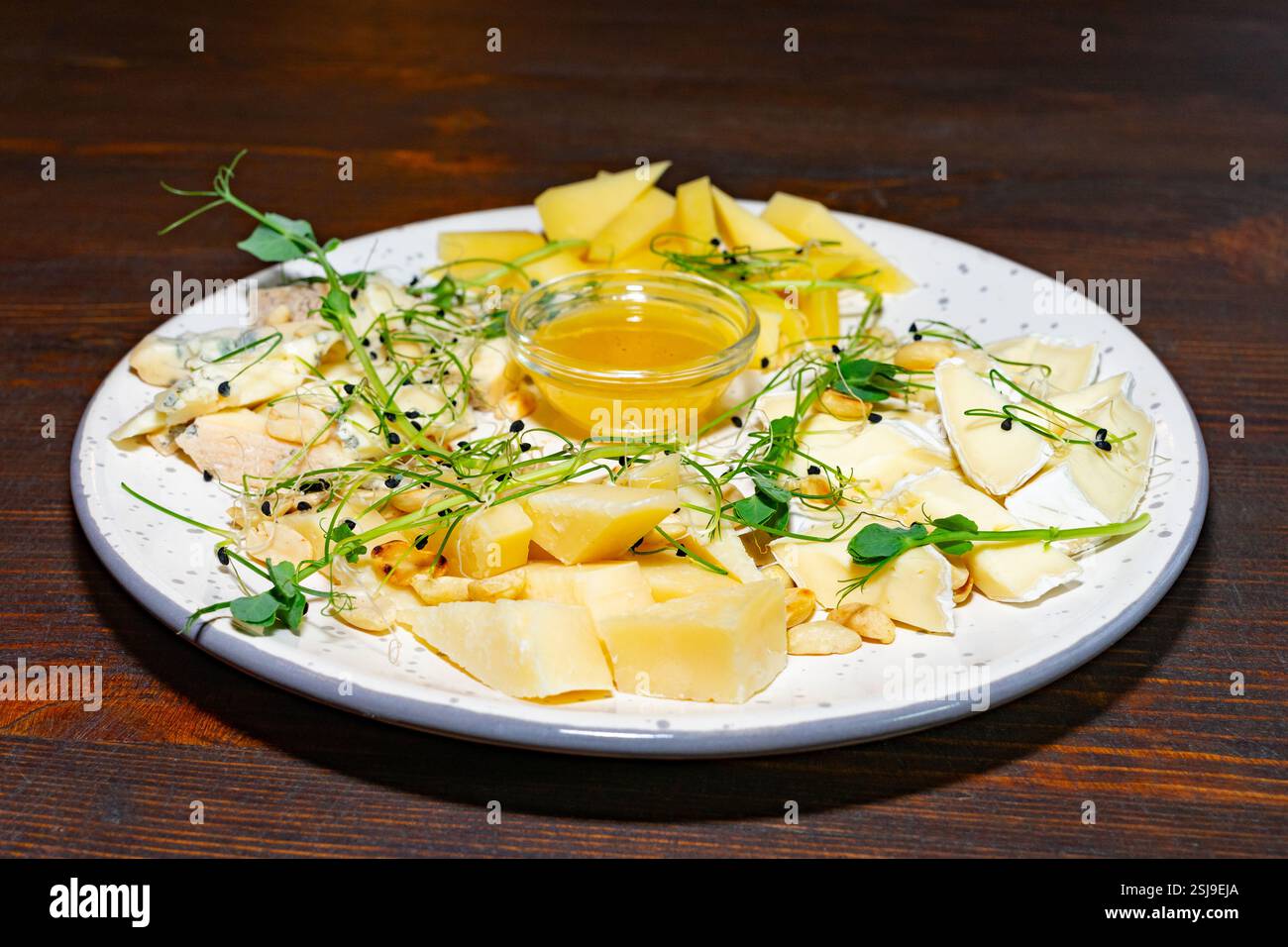 Eine vielfältige Auswahl an Käsesorten ist wunderschön auf einem runden Teller angeordnet. Begleitet von Honig und garniert mit frischen Kräutern ist dieses Gericht perfekt für Stockfoto