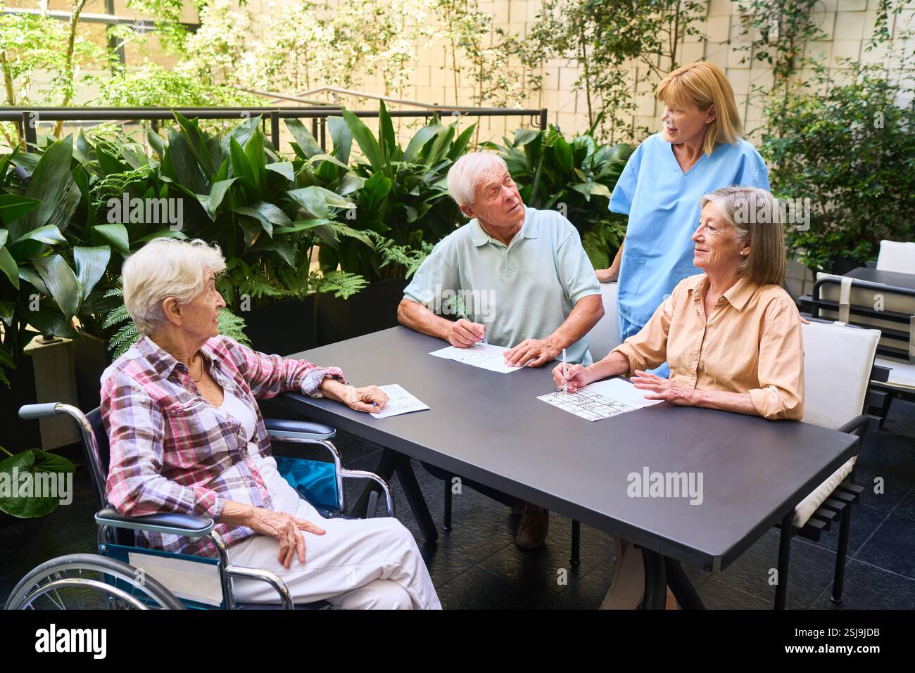 Ältere Erwachsene, die an Freizeitaktivitäten mit einer Betreuungsperson in einer ruhigen Umgebung im Freien teilnehmen und dabei soziale Interaktion und Wohlbefinden fördern Stockfoto