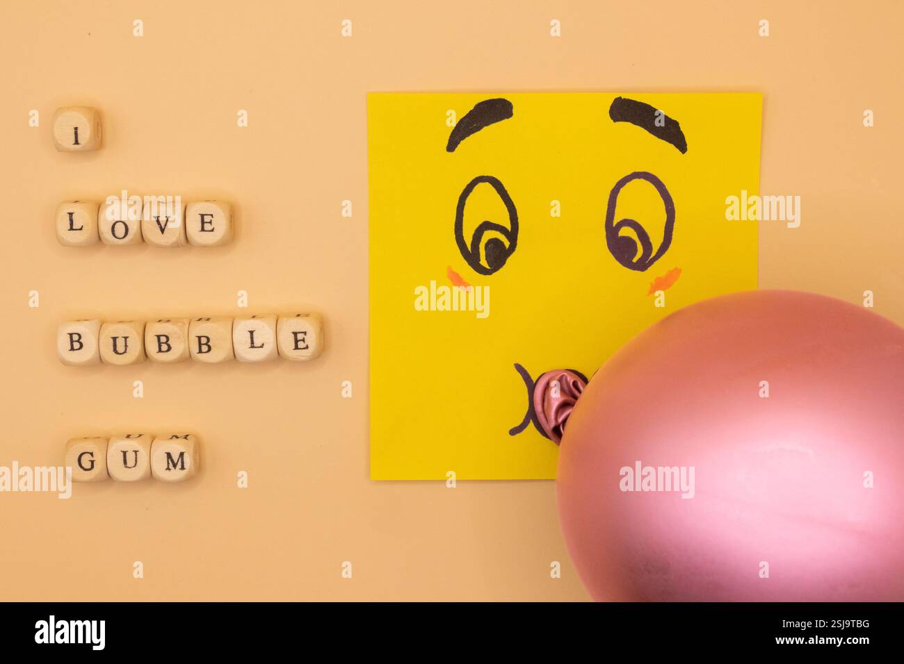 Ein Konzept eines Emoticon Notizblocks, das eine Blase Kaugummi auf beigem Hintergrund für den National Bubble Gum Day bläst. Stockfoto