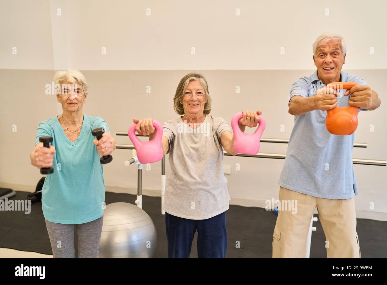 Drei Senioren nehmen Kraftübungen mit Kettlebells und Kurzhanteln in einem Rehabilitationszentrum Teil. Sie zeigen Entschlossenheit an Stockfoto