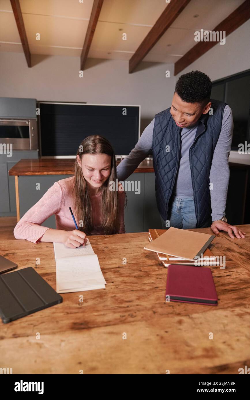 Mann Assisting Girl (12-13) schreibt in Notizblock Stockfoto