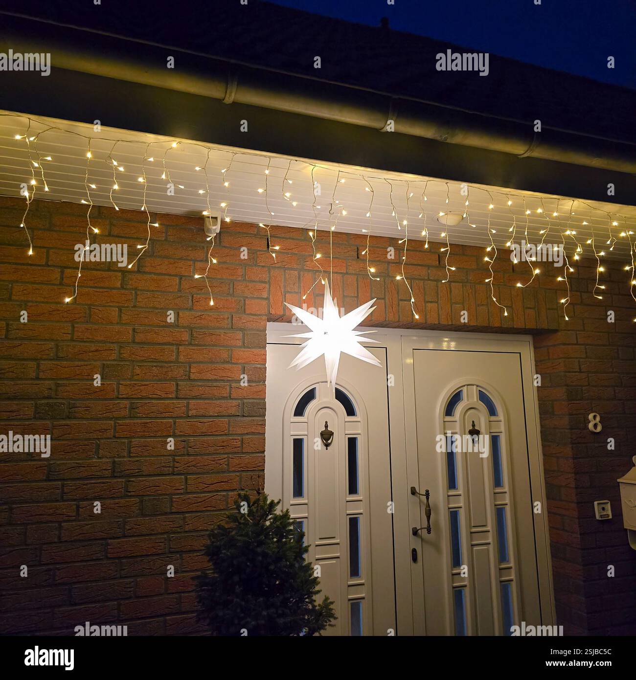 Die charmante Eingangstür ist wunderschön mit funkelnden Lichtern und einem strahlenden Stern verziert, um festliche Feierlichkeiten zu unterstreichen Stockfoto