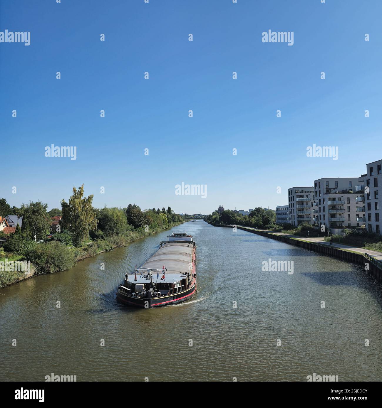Ein atemberaubender Blick auf einen sich windenden Fluss mit einem Lastkahn, der sanft durch eine ruhige, friedliche Landschaft im Mittellandkanal Hannover gleitet Stockfoto
